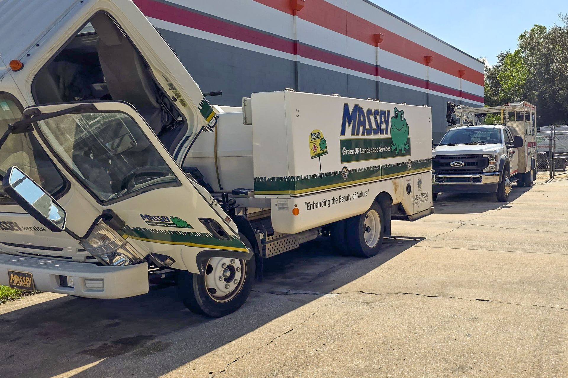 Damaged white delivery truck parked beside a striped building, with another truck behind it.