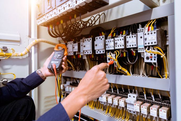 Un elettricista utilizza una pinza amperometrica digitale per testare i circuiti di un complesso quadro elettrico industriale pieno di cavi, relè e interruttori.