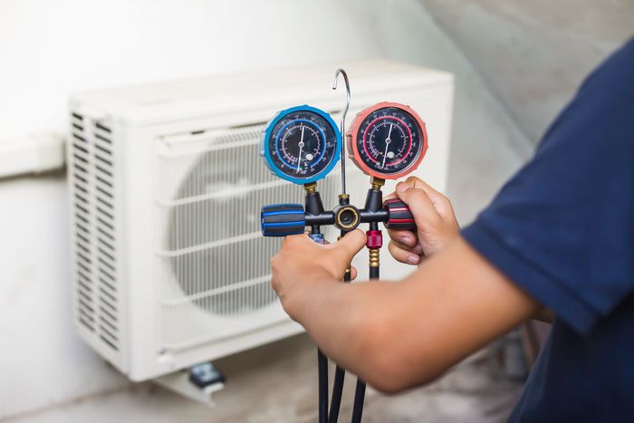 Un tecnico utilizza un set di manometri per impianti di climatizzazione, uno rosso e uno blu, per controllare un'unità esterna di condizionamento dell'aria di colore bianco.