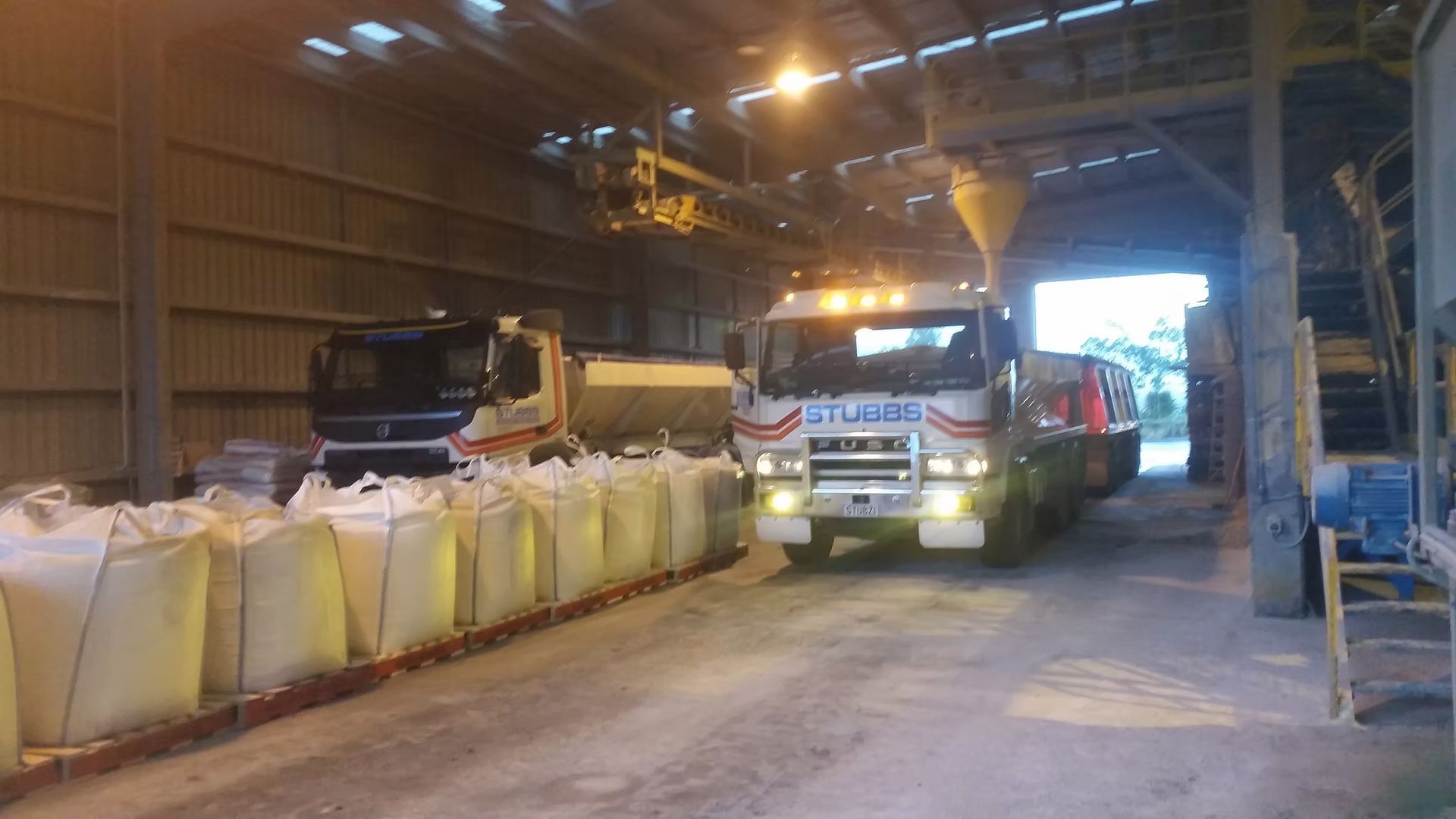 Truck inside a warehouse loading or unloading large white bulk bags near a conveyor line