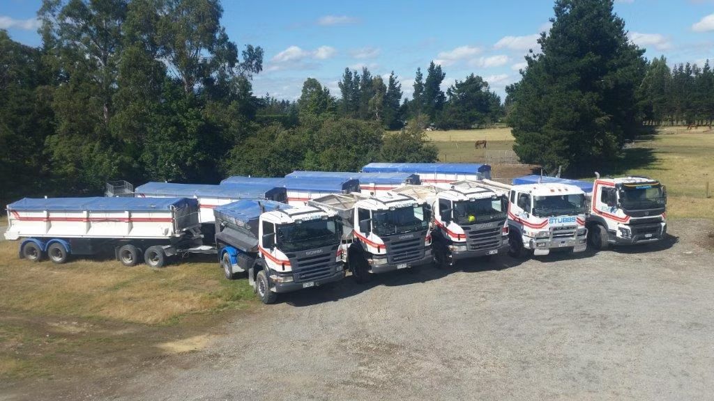 Lineup of white tanker trucks and trailers parked on a gravel lot under a blue sky