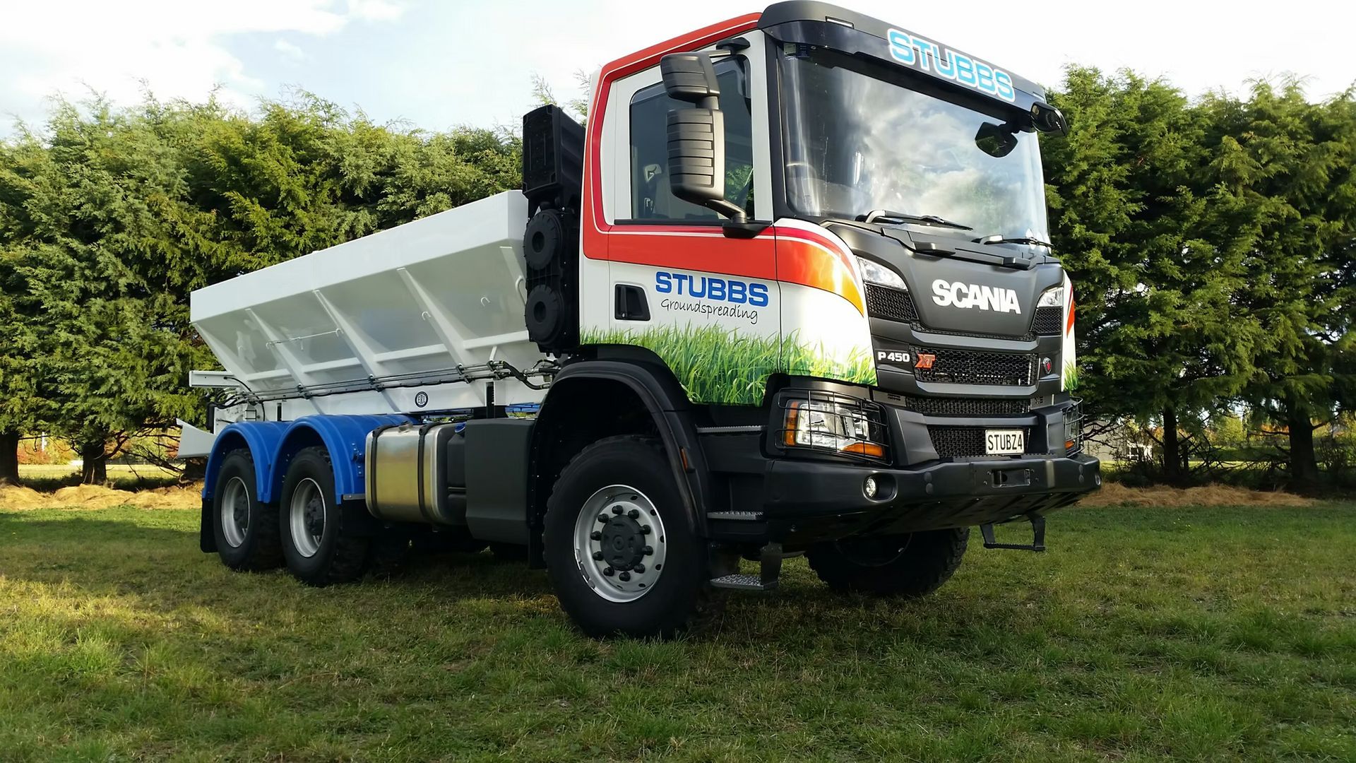 Large white Scania dump truck with red cab parked on grass in an orchard