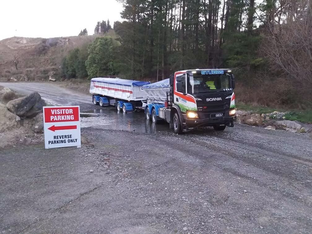 Truck towing a trailer on a muddy rural road beside a red warning sign