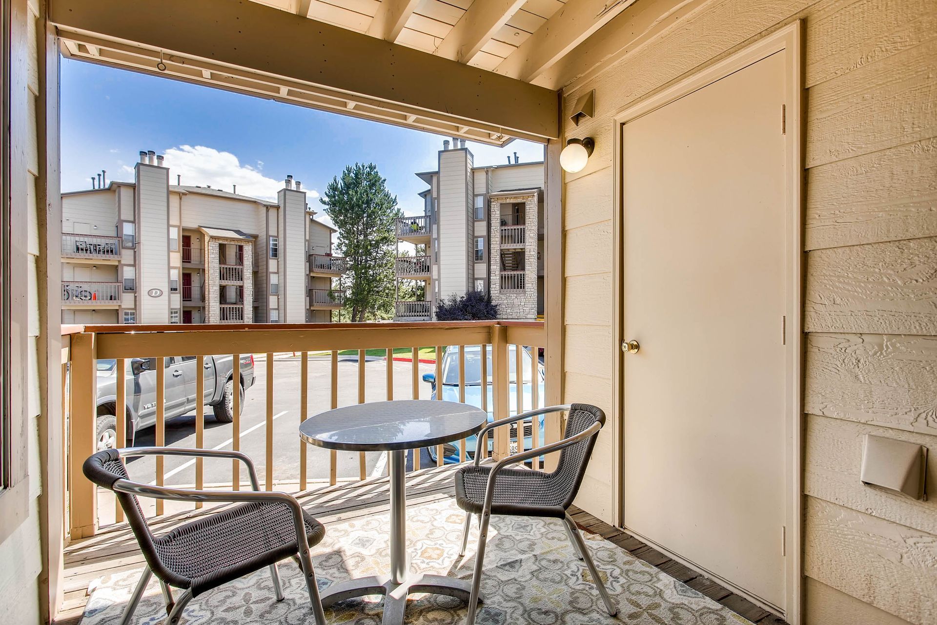 Balcony with table and chairs overlooking buildings and street. Door on right.