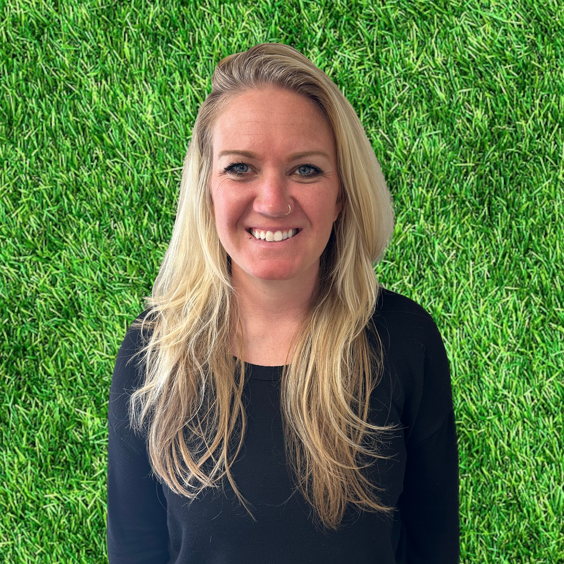 A woman in a black shirt is smiling in front of a green grass background.