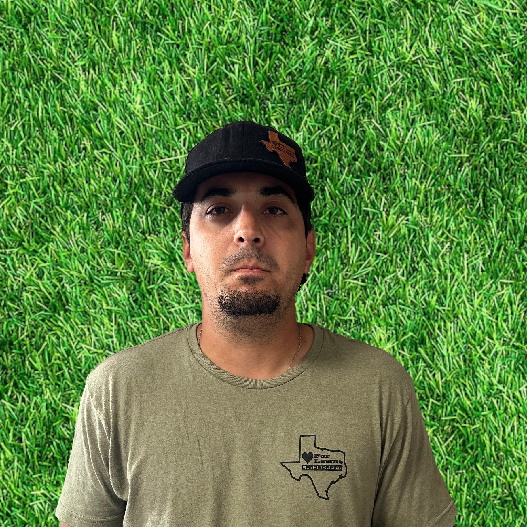 A man wearing a hat and a t-shirt is standing in front of a wall of grass.