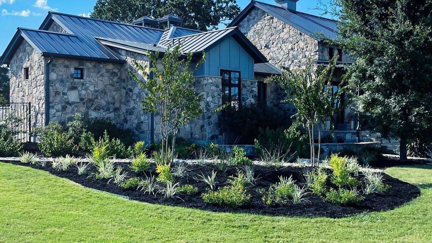 A large stone house with a metal roof and a lush green lawn in front of it.