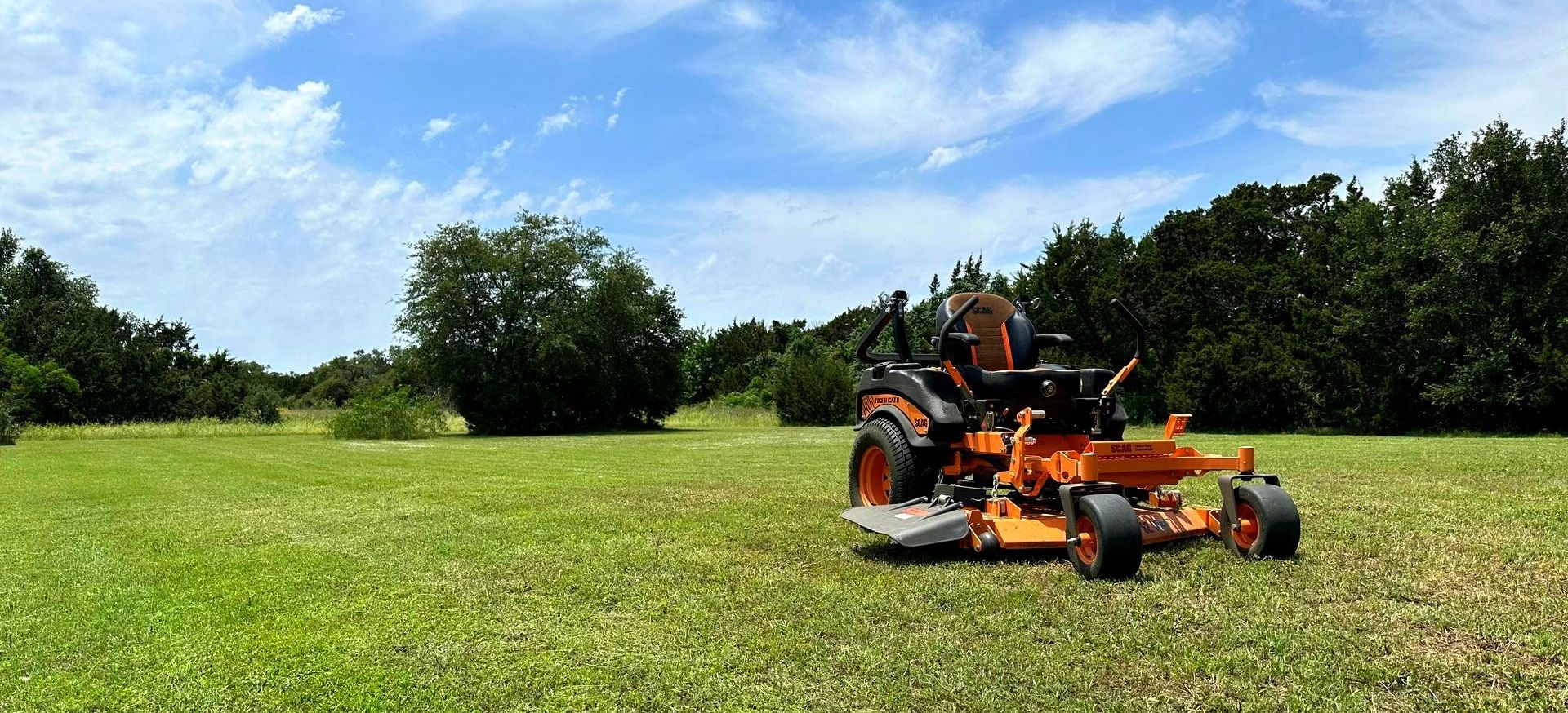 An orange lawn mower is sitting in the middle of a lush green field.