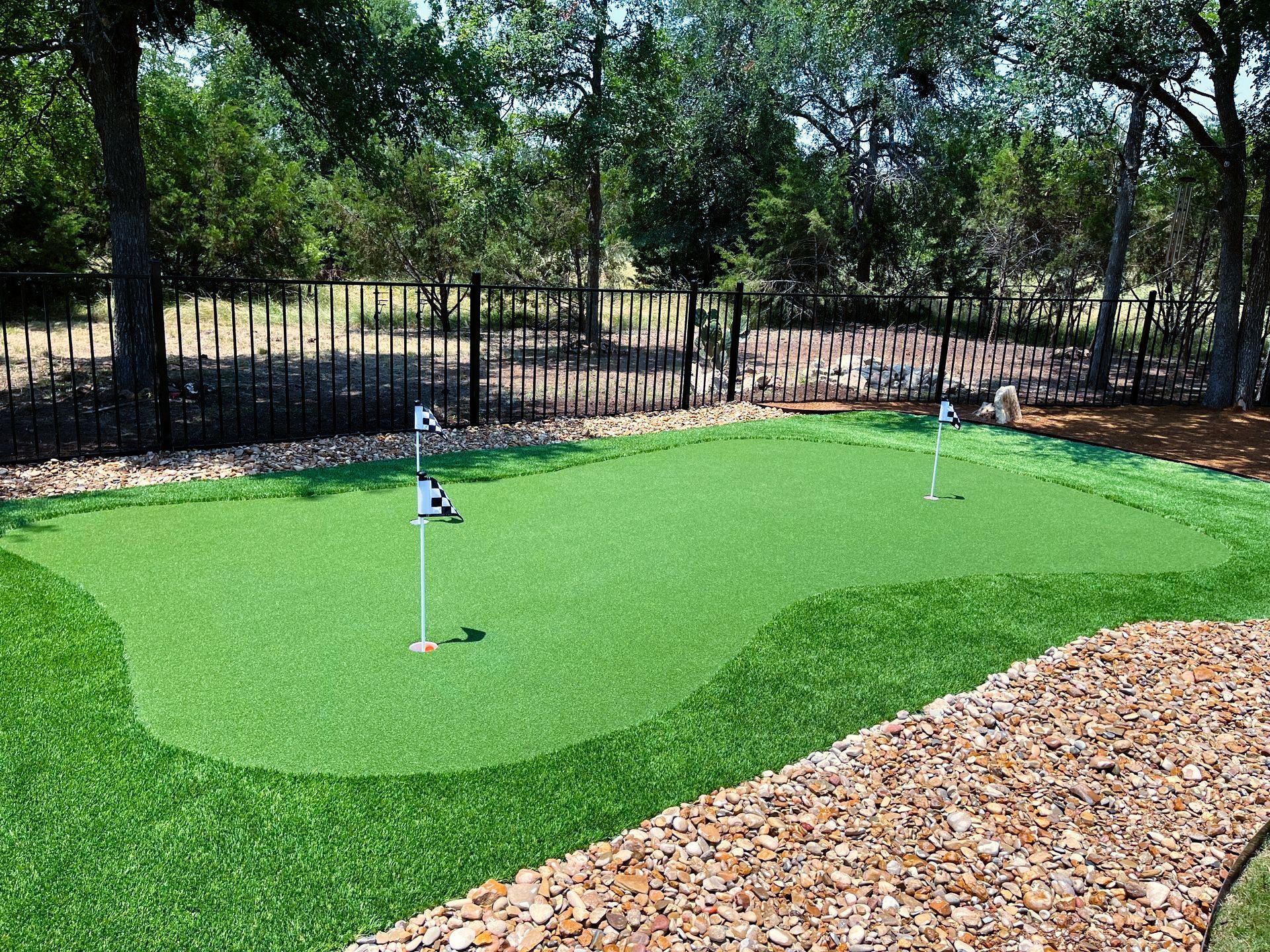 A putting green in a backyard with a fence and trees in the background.