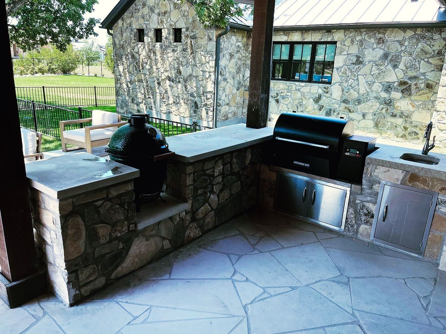 A patio with a grill and a sink in front of a stone building.