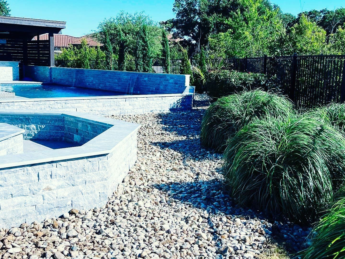 A swimming pool is surrounded by rocks and bushes in a backyard.