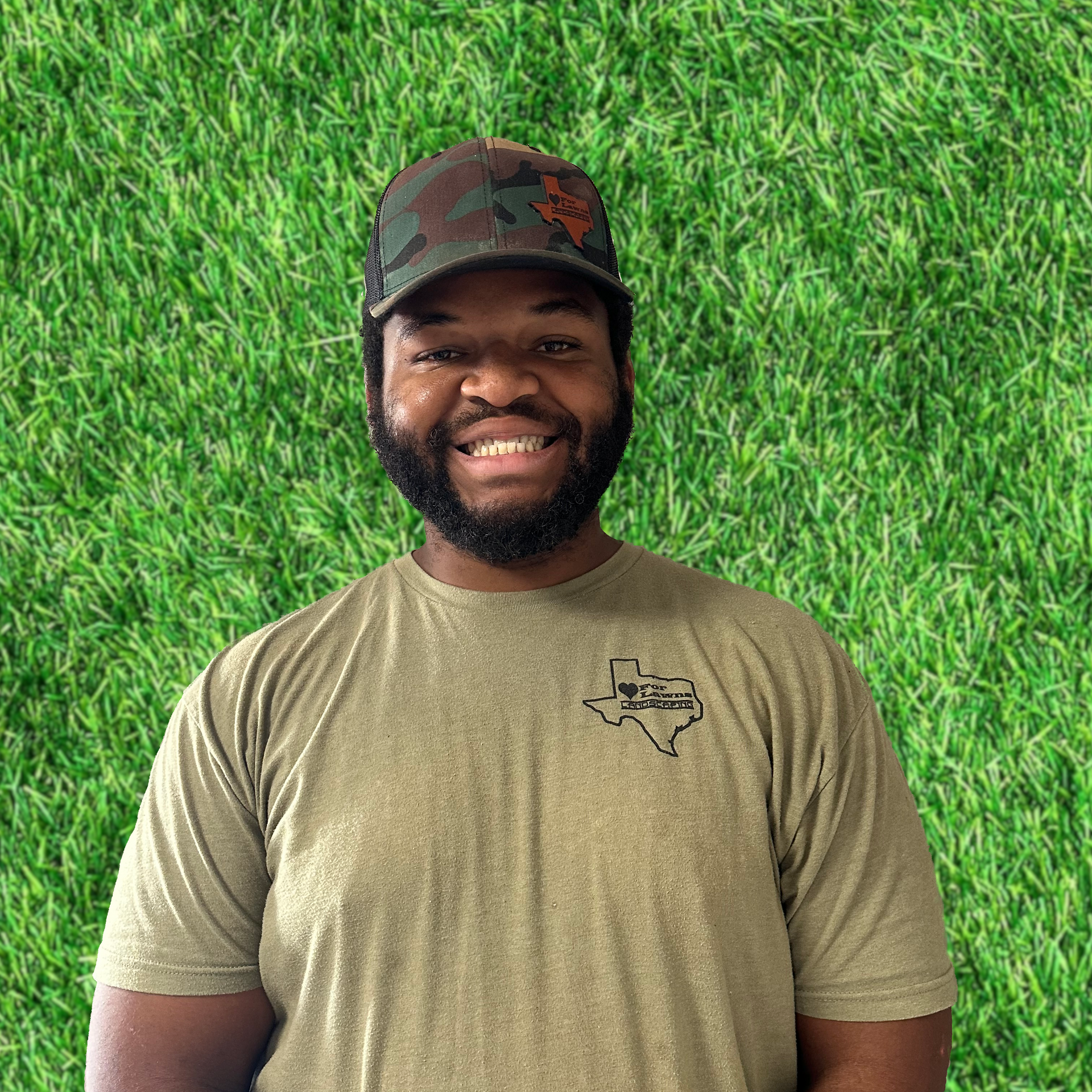 A man wearing a hat and a t-shirt is standing in front of a wall of grass.