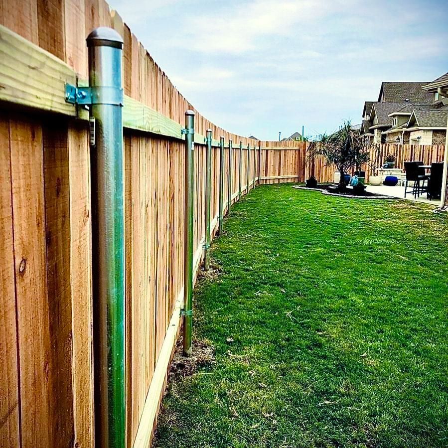 A wooden fence surrounds a lush green lawn in a backyard.