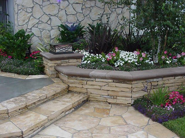 Stone garden steps beside a raised flower bed with pink and white blooms against a stone wall