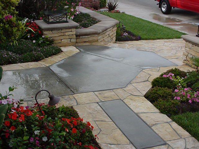 Front walkway with decorative concrete, stone borders, and flower beds leading to a porch and curb.