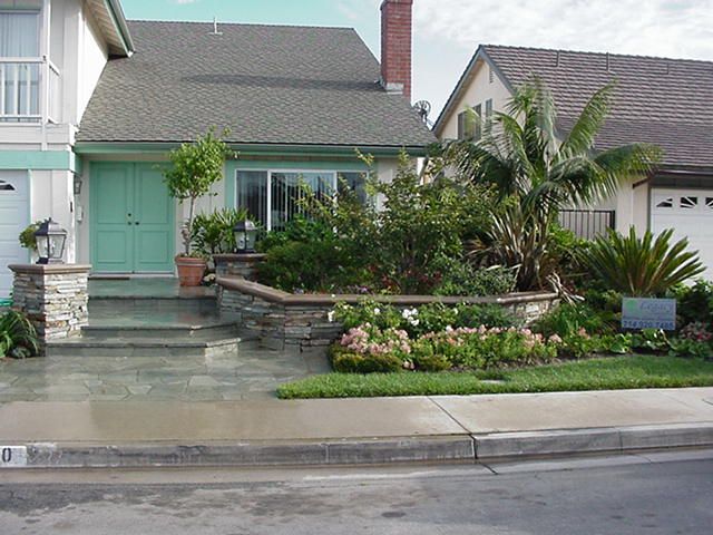 Single-story house with mint-green front door, lush garden, and palm trees by the curb