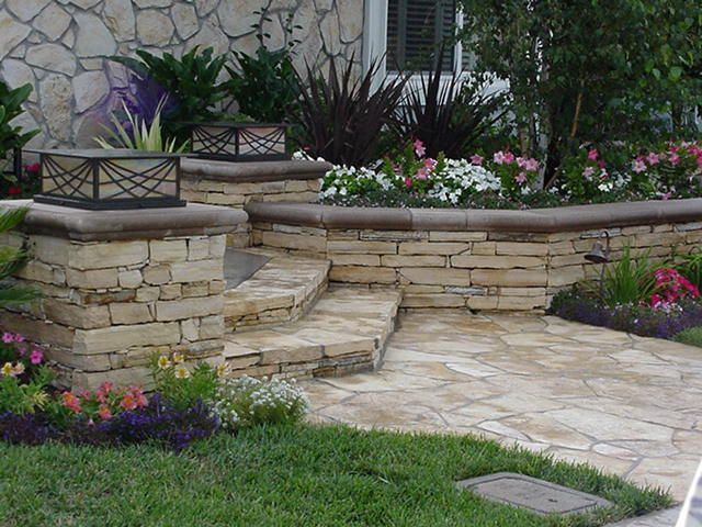 Stone patio steps and flower beds in a landscaped garden with green lawn and potted plants