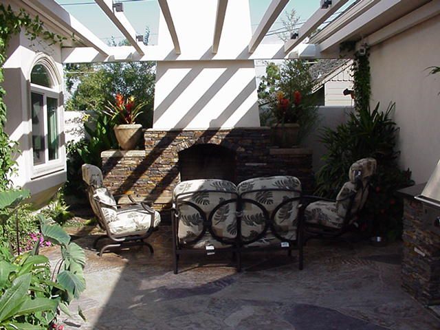 Covered patio with wicker seating, potted plants, and stone steps in bright sunlight