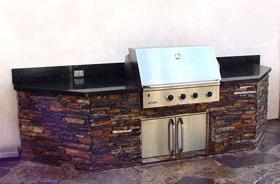 Outdoor stone and stainless steel grill island with black countertops and a built-in grill panel