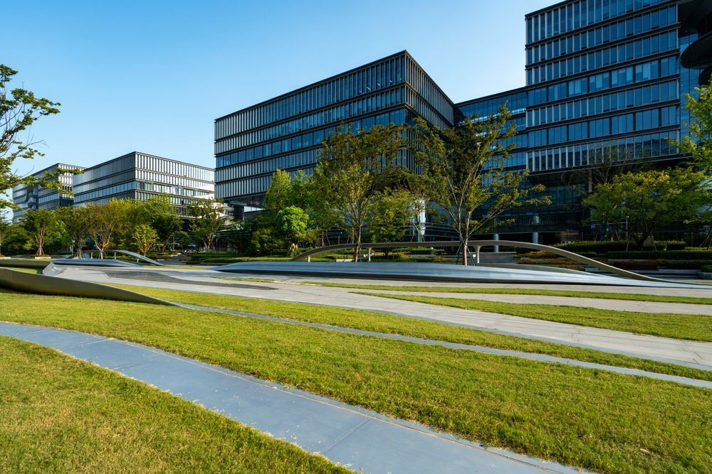 Modern glass office buildings beside a landscaped lawn and curved paths under a clear blue sky