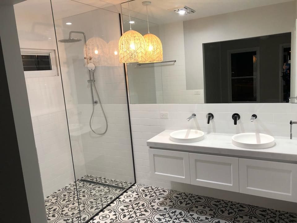 Modern bathroom with glass shower, patterned tile floor, double vanity, and woven pendant lights