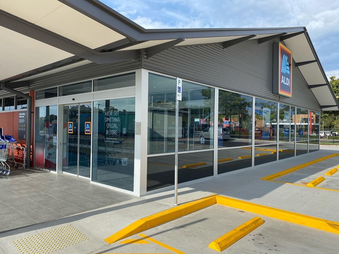 Modern storefront with glass walls and covered entrance, seen from parking lot with yellow curbs.