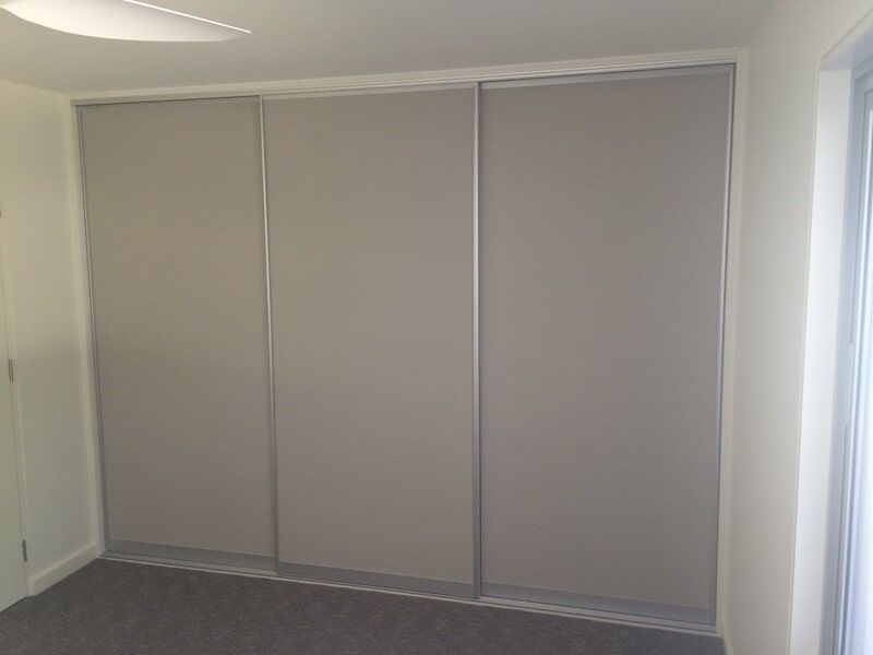 Gray sliding closet doors in a sparsely furnished room with white walls and carpeted floor