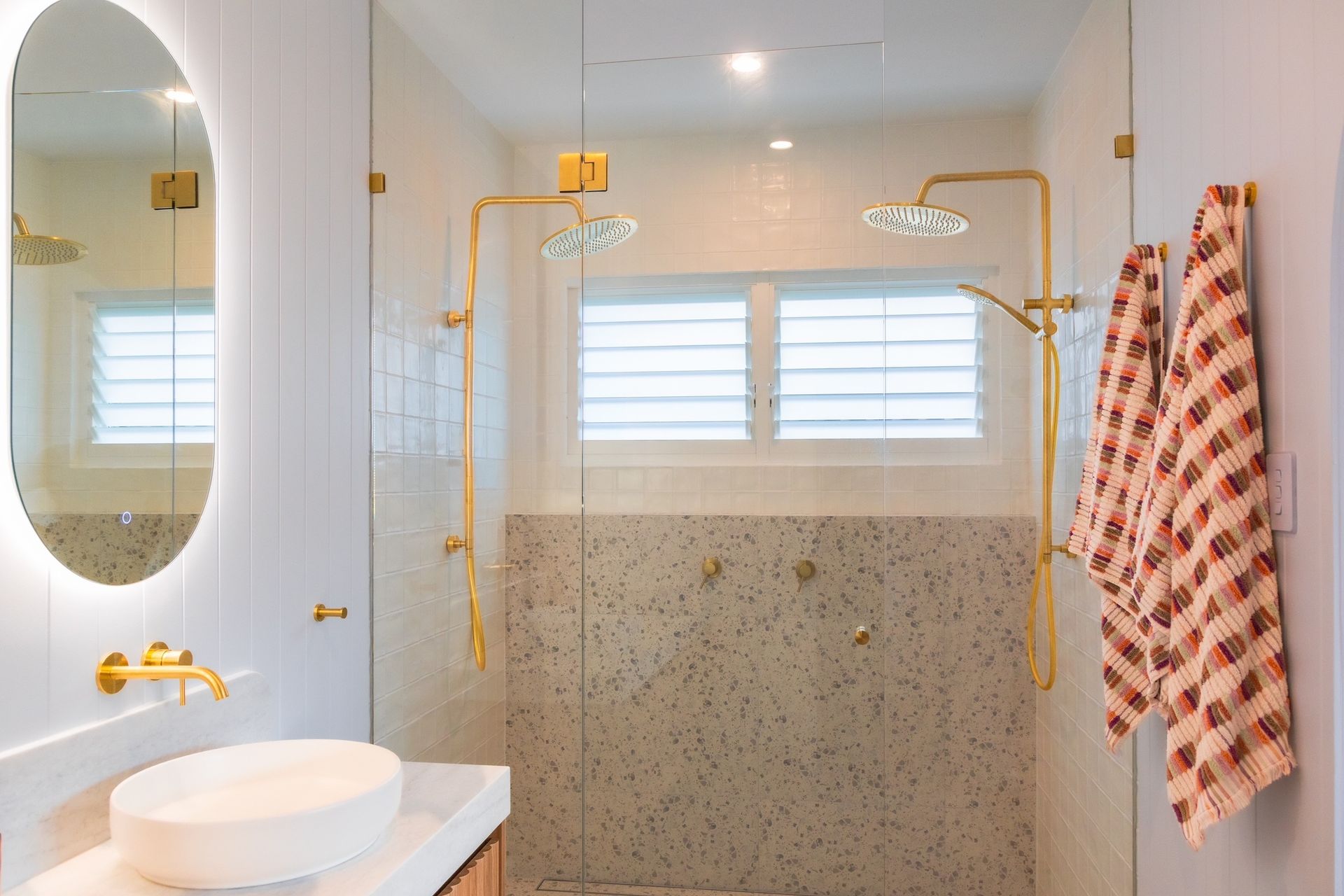Glass shower enclosure in a modern bathroom with gray tile and white fixtures