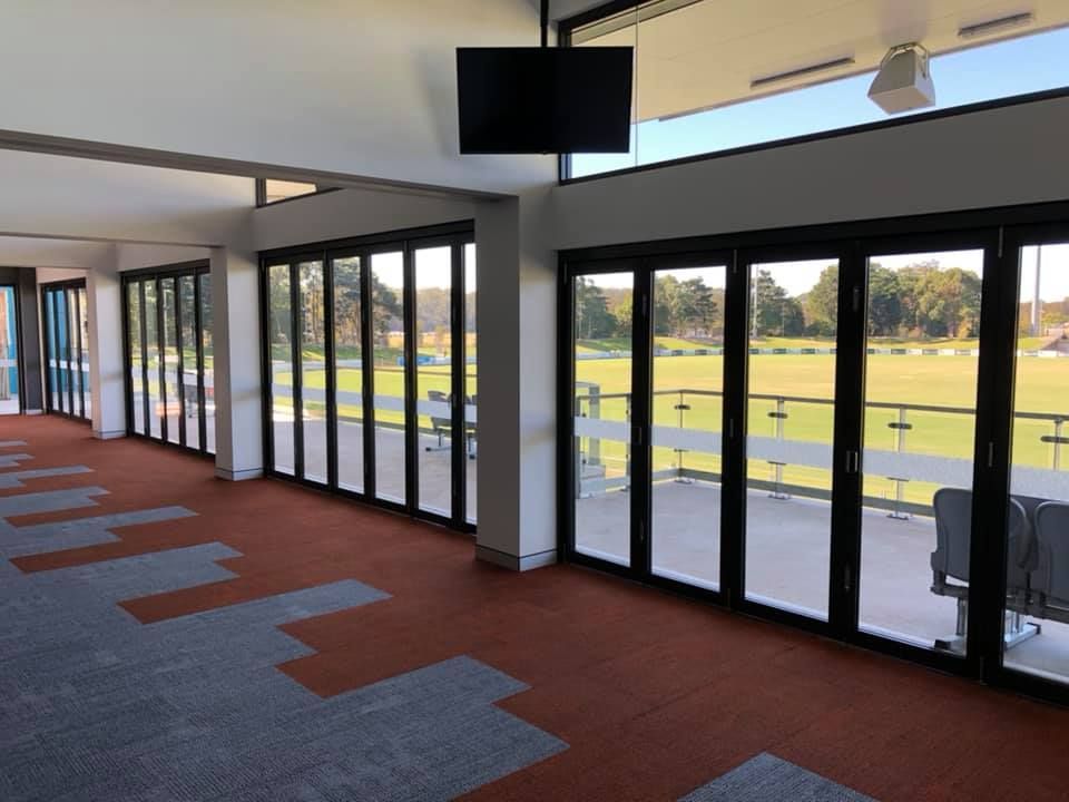 Empty indoor corridor with glass doors, red carpet, and a view of a grassy field outside