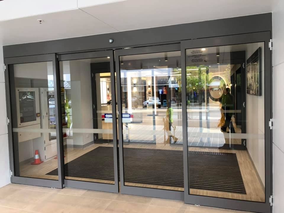 Glass storefront entrance with sliding doors and dark mats on the floor