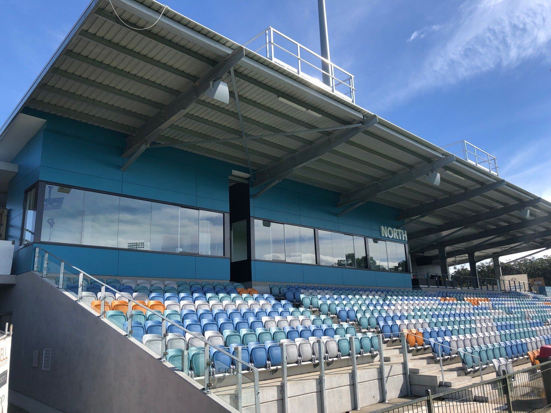 Empty blue-and-white stadium seating under a covered grandstand with glass-fronted boxes