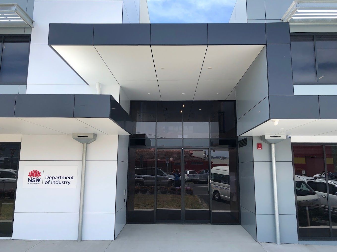 Modern building entrance with glass doors, gray awning, and a small sign on the left