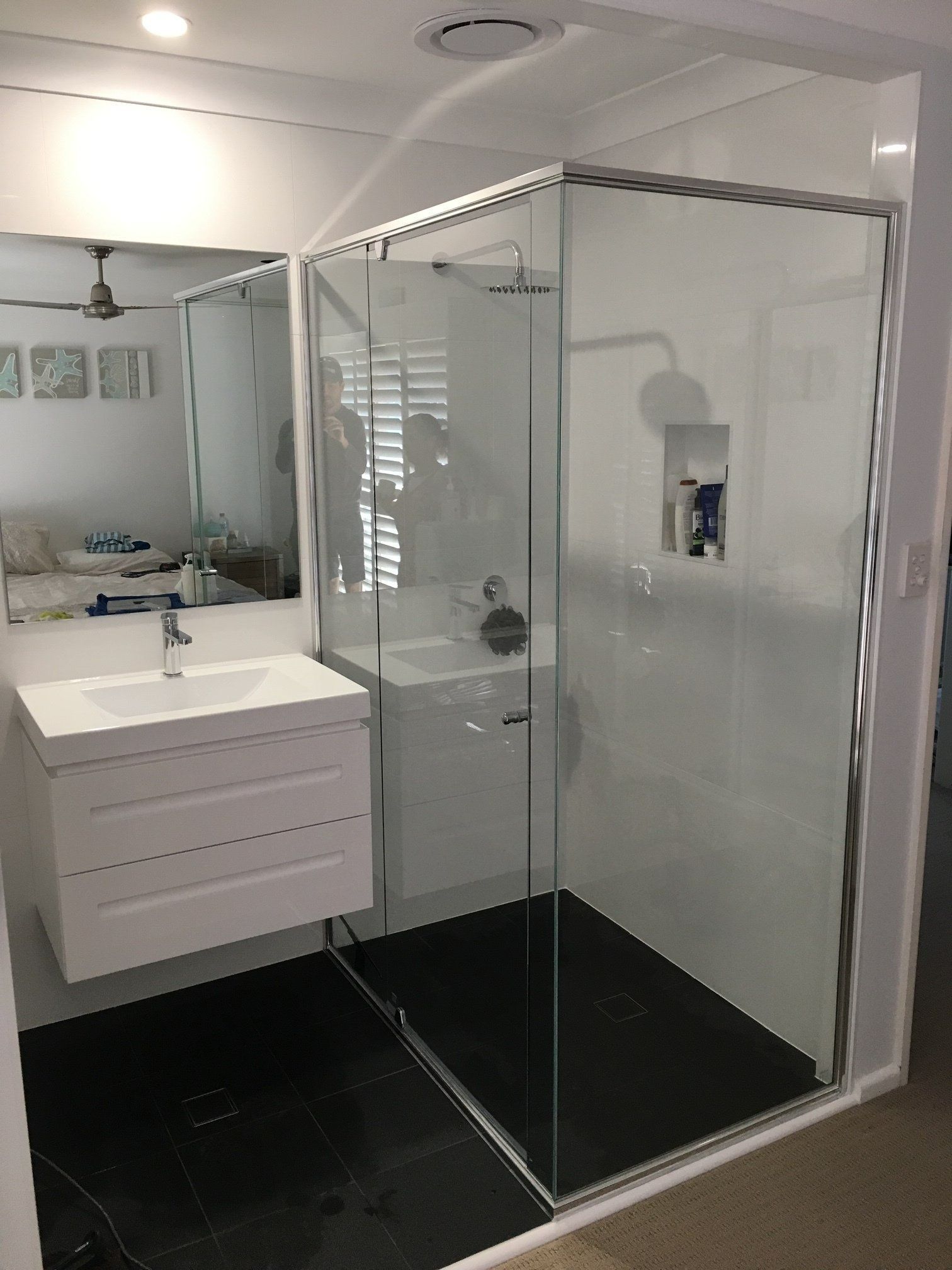 Modern bathroom with glass shower enclosure, white vanity, mirror, and black tile floor