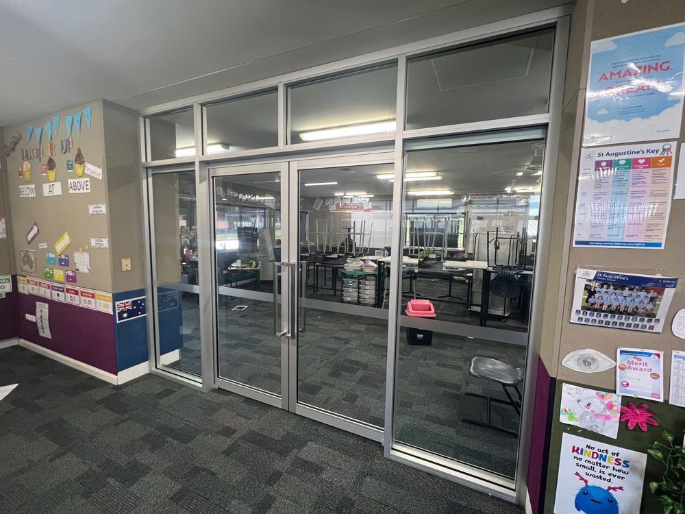 Empty glass entrance to a gym, with posters on the walls and exercise equipment visible inside.