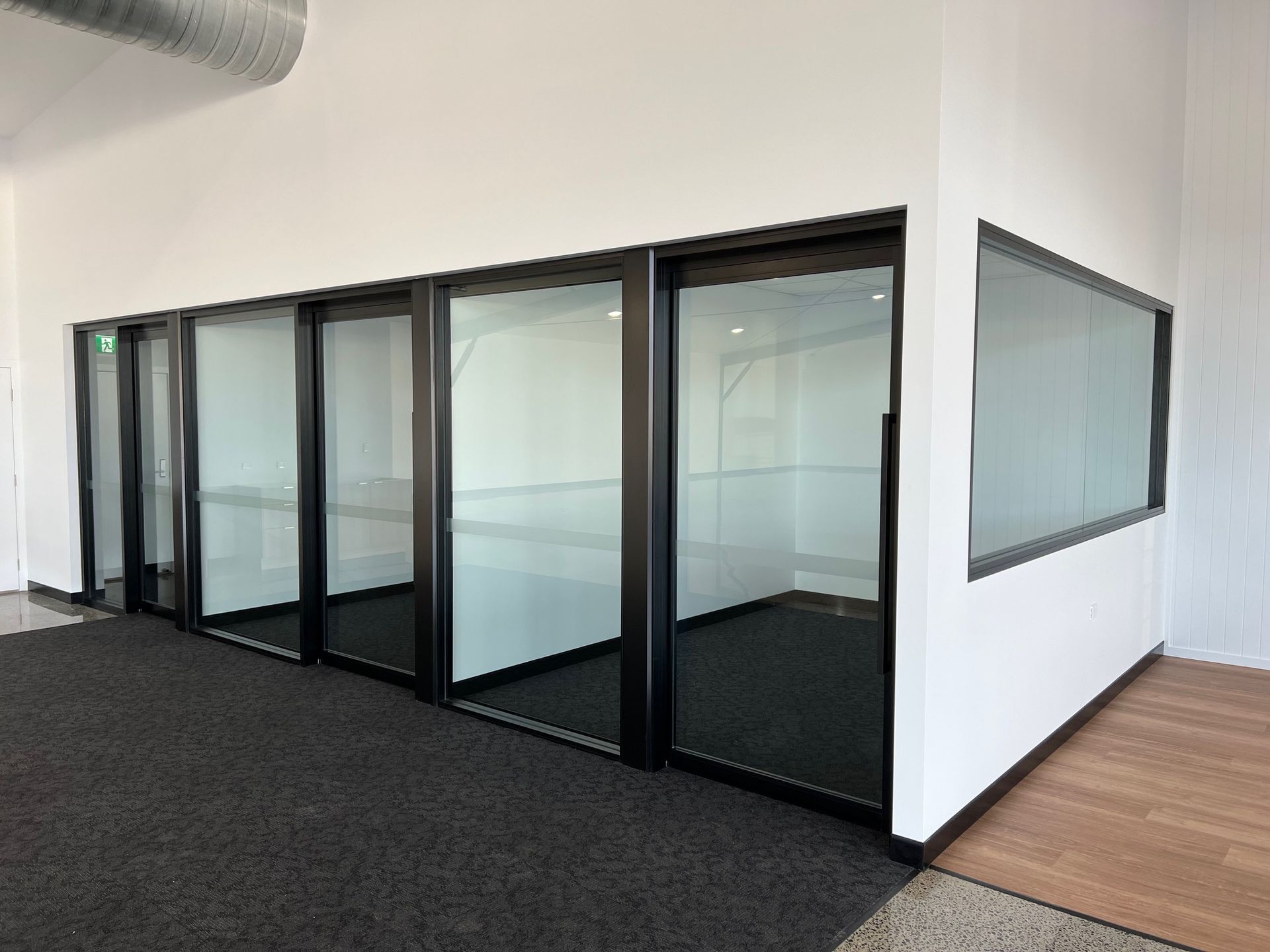 Modern office hallway with glass-walled meeting rooms and black carpet flooring