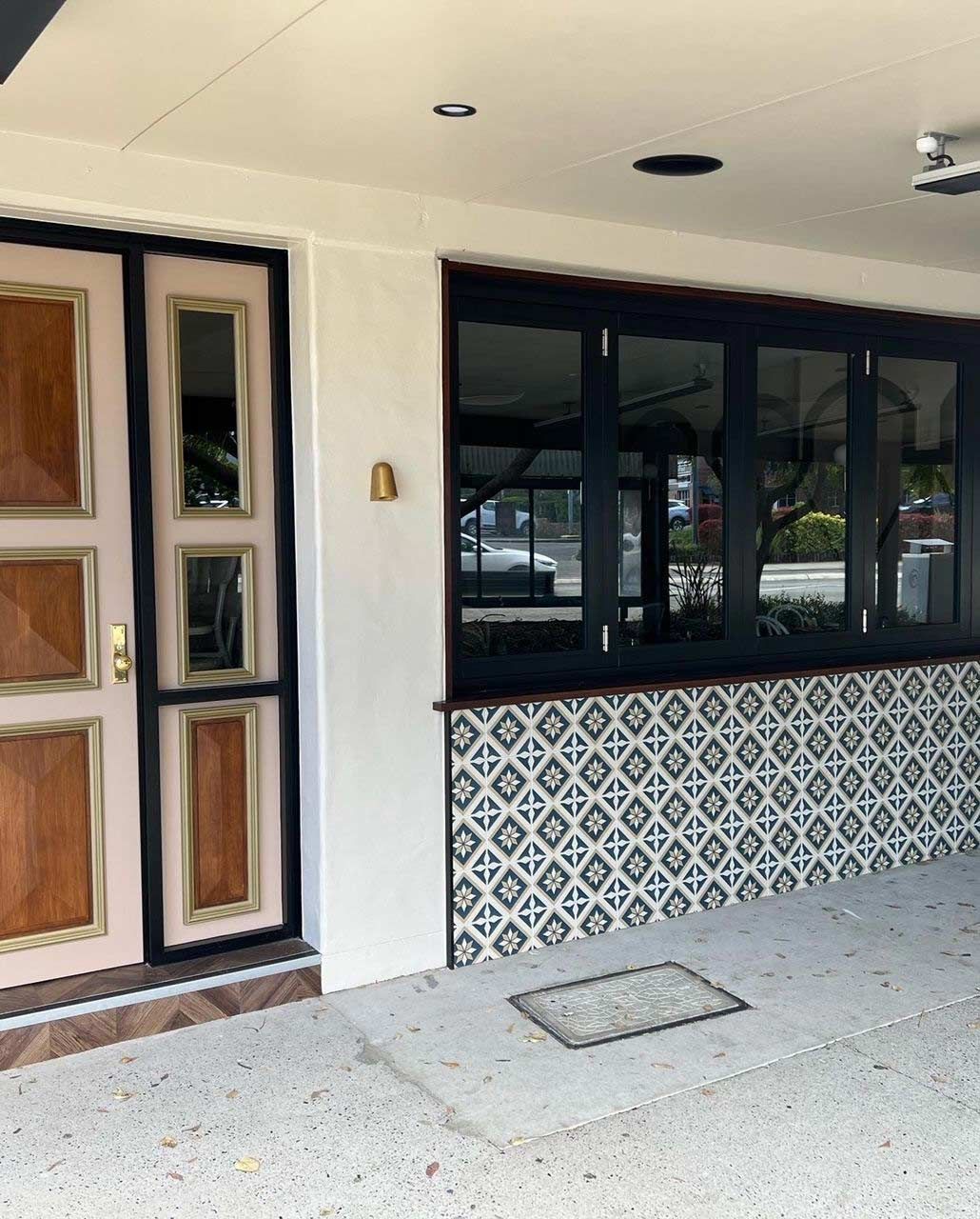 Exterior of a building with a wooden door, large window, and patterned tile wall under a covered walkway