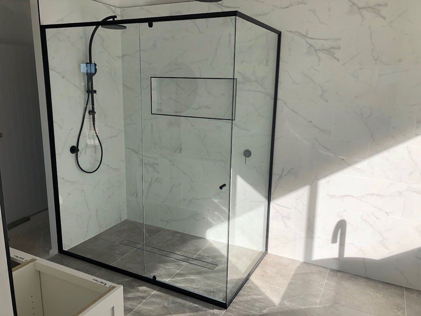 Black-framed glass shower enclosure with wall-mounted shower head and marble-look tile walls