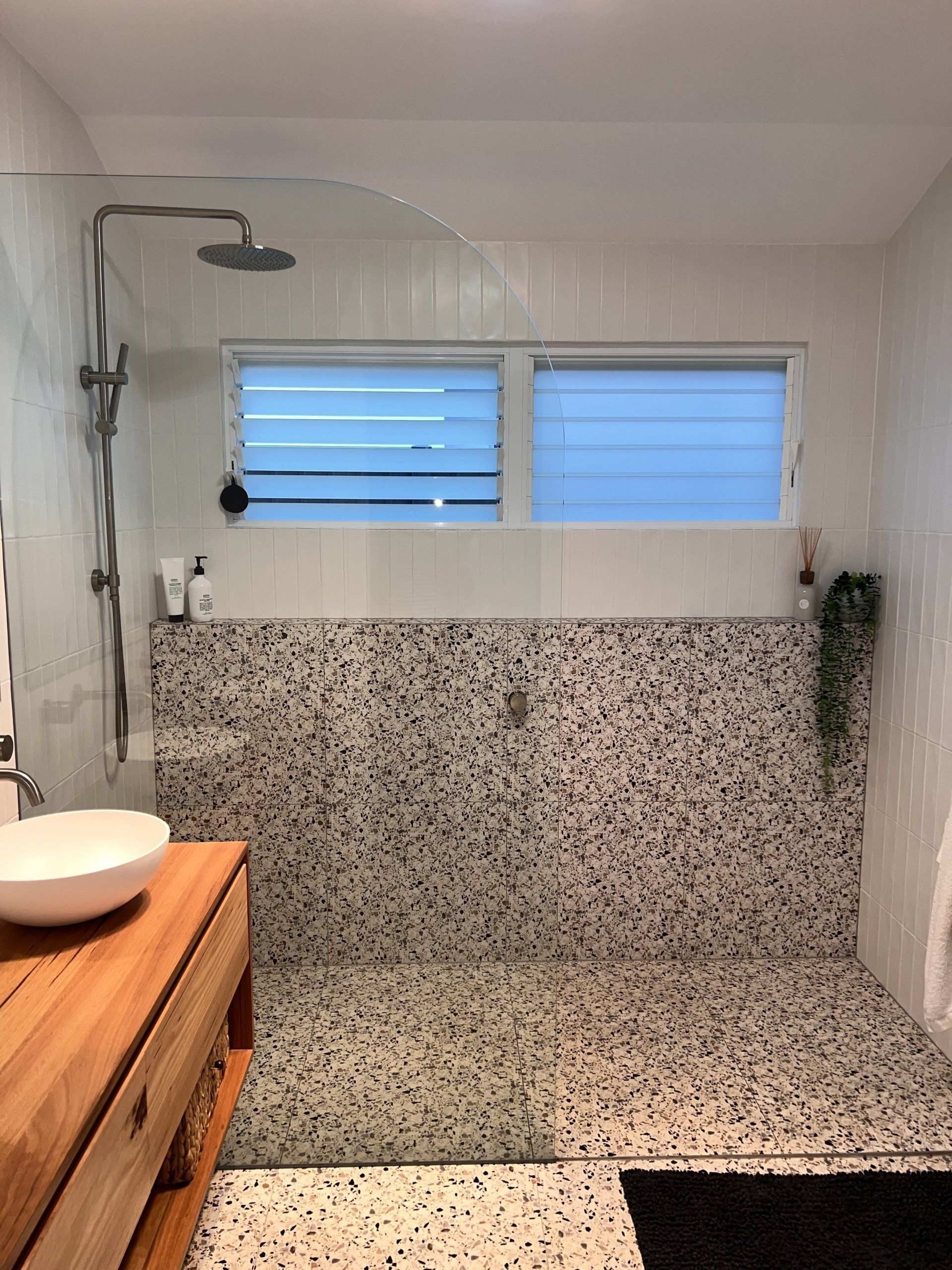 Modern bathroom shower with terrazzo walls, a window, and a wooden vanity with a white sink