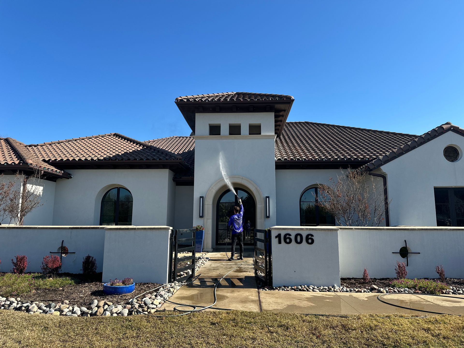 A man is cleaning the front of a white house with a pressure washer.