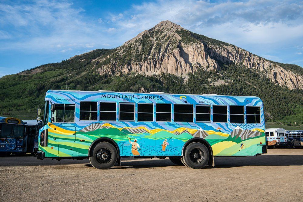 Mountain Express bus with mountain scene, blue and green, in front of a large mountain.