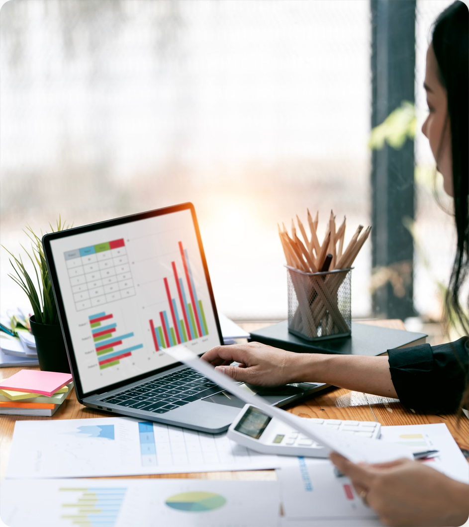 Woman analyzing financial data on laptop, with calculator and papers on desk.