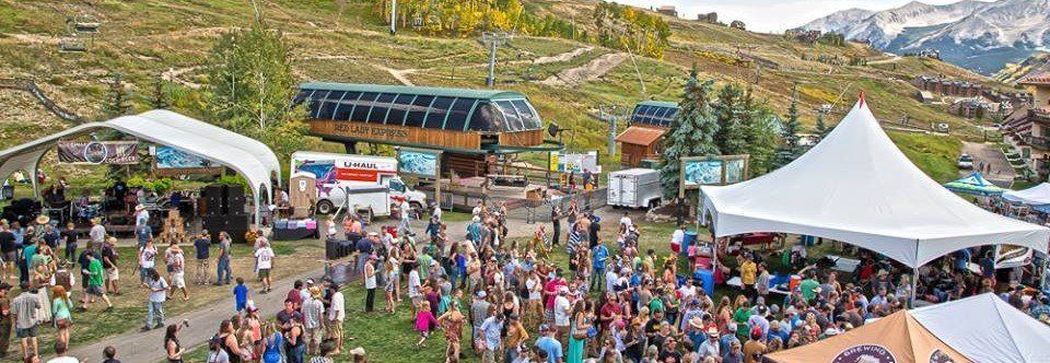 Festival with large crowd, tents, food vendors, and ski lifts in a mountain setting.