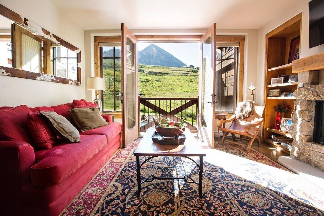 Cozy living room with red couch, open doors to mountain view, and floral rug.