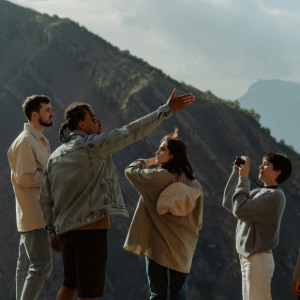 A group of five people stand outdoors on a mountainside, looking up as one person points toward the sky.