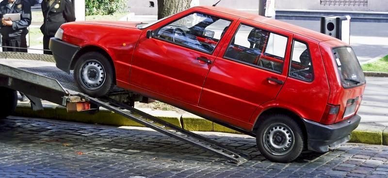 Red car being towed onto a tow truck. A few people stand in the background.