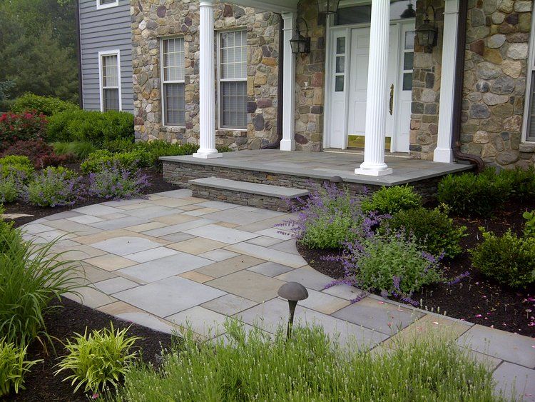 A stone walkway leading to a house surrounded by trees and bushes.