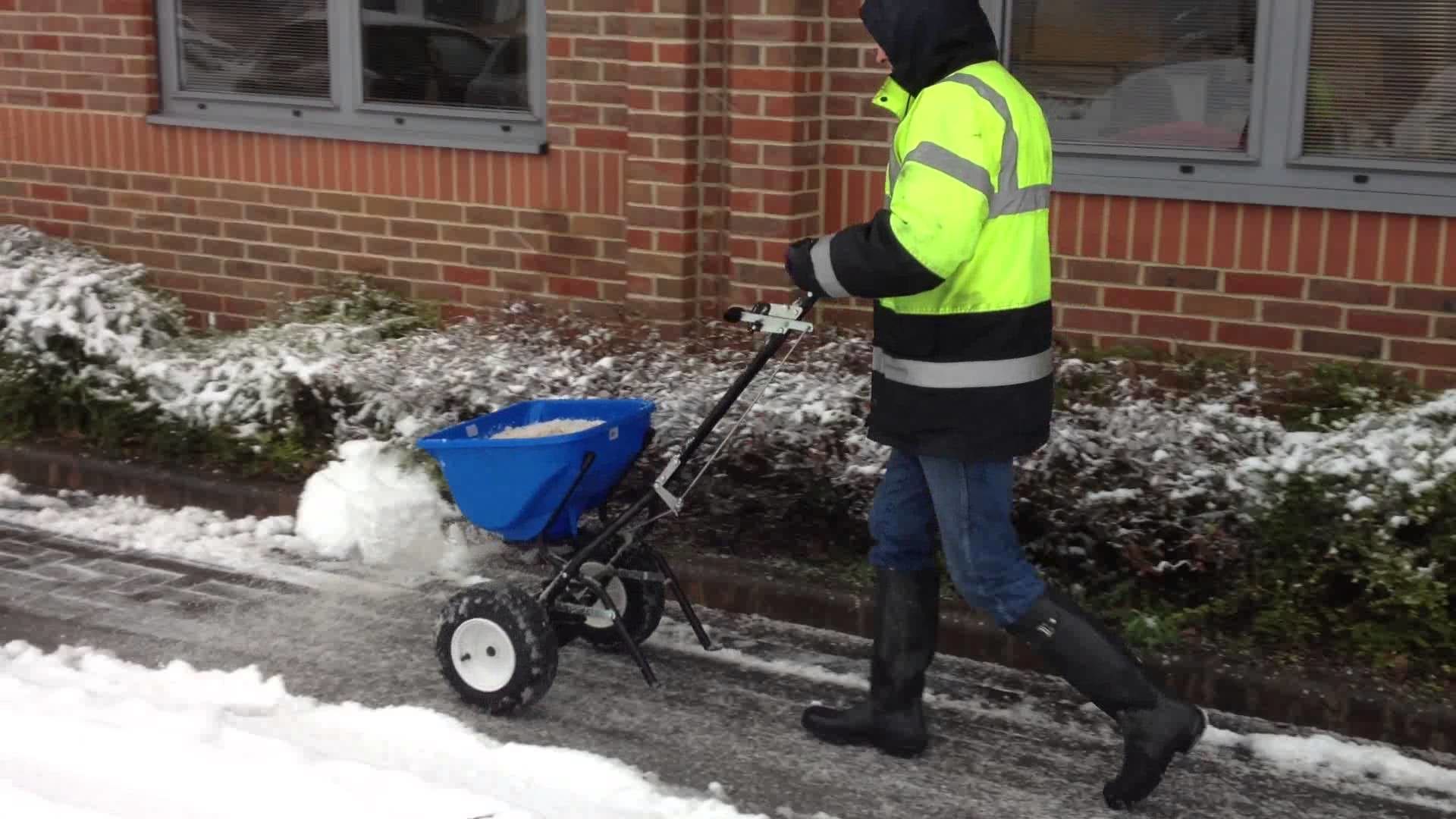 Professional worker spreading de-icing salt along a snowy walkway outside a building