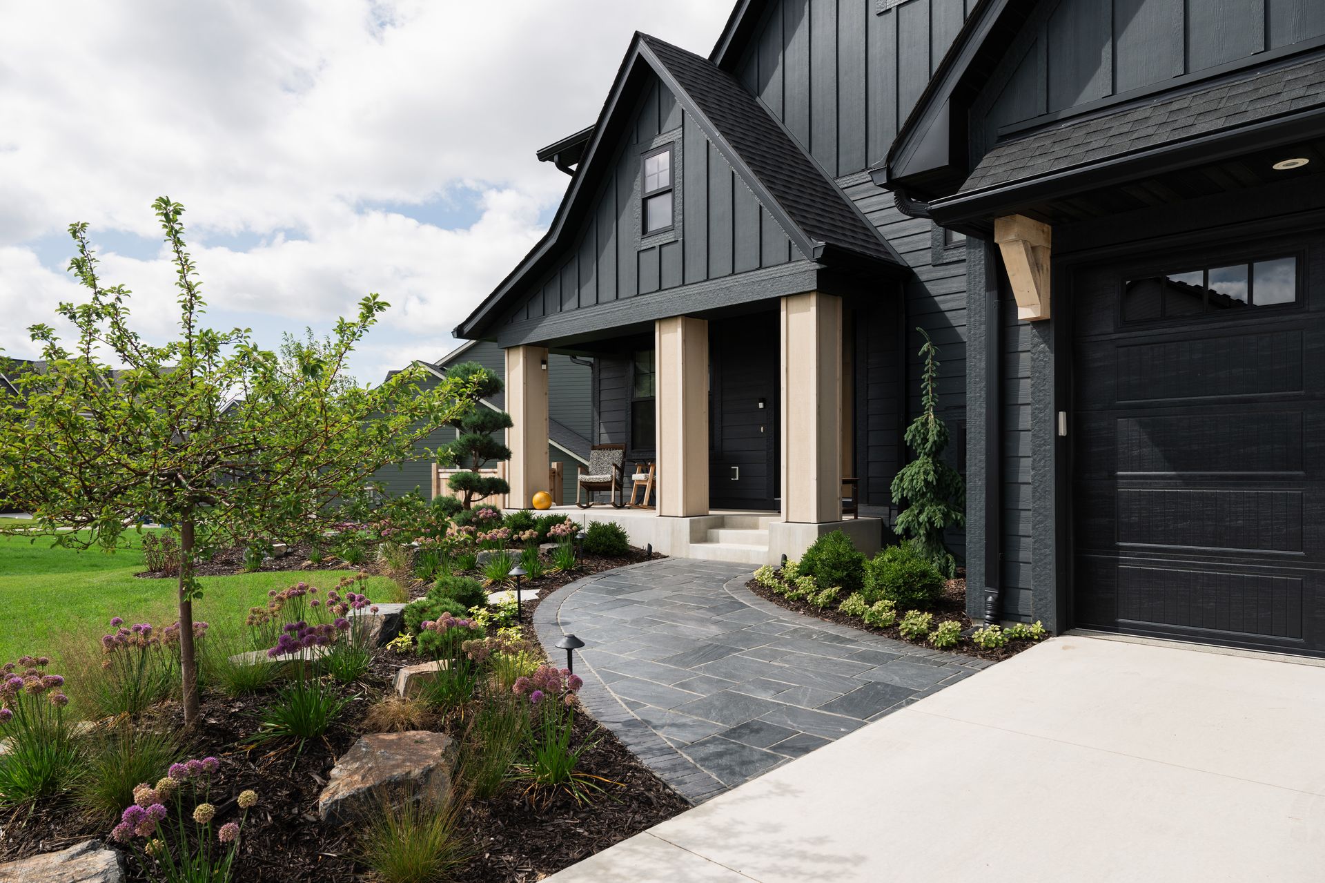 Green lawn and colorful flowerbed lead to a white-doored home with a porch, hanging flowers.