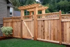 Wooden fence with gate, arched top, and trellis. Brown wood in a green lawn setting.