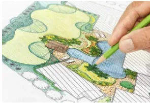 Hand with green pencil drawing a colorful landscape design plan.